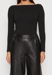 Musta pitkähihaisen yläosa leveällä venekaula-aukkolla, yhdistetty korkeavyötäröisiin mustiin nahkahousuihin, joissa on sileä pinta ja joustava vyötärönauha.