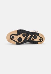 Semelle d'une basket Puma beige et noire avec motifs d'adhérence circulaires et logo Puma centré sur la semelle intermédiaire.