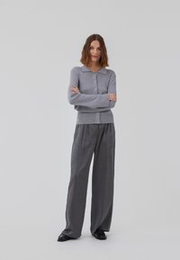 Gray knitted cardigan with a round collar and button closure, paired with loose gray trousers and black shoes. Smooth texture, casual design.
