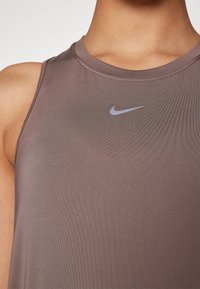 Gros plan sur une personne portant un haut sans manches mauve de Nike avec un petit logo swoosh gris sur la poitrine.