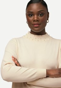 Beige svetr s ribkovou texturou a perlov�ými akcenty kolem vysokého límce. Dlouhé rukávy a přiléhavý střih.