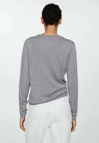 Sivi džemper dugih rukava s okruglim izrezom, mekan na dodir, opuštenog kroja i glatkim leđima, kombiniran s bijelim hlačama.