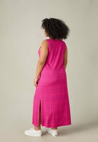 Różowa, bezrękawnikowa sukienka maxi o wzorzystej fakturze i bocznym rozcięciu, w połączeniu z białymi trampkami. Projekt jest luźny i o średniej długości.