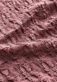 Tissu de dentelle rose poussiéreuse détaillé avec des motifs floraux et géométriques, montrant la texture et de doux plis.