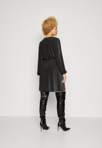 Μαύρο γυαλιστερό φόρεμα με μακριά μανίκια, τονισμένη μέση και κρόσσι μήκους γονάτου, σε συνδυασμό με μαύρες μπότες με τακούνι έως το μηρό.