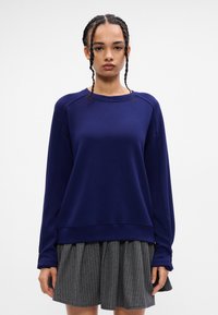 Sötétkék pulóver hosszúujjakkal, bordázott kerek nyakkivágással és laza szabással. Simább textúrával és diszkrét varrási részletekkel rendelkezik.