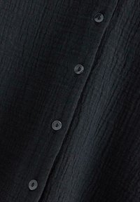 Tessuto nero con una texture ondulata, caratterizzato da bottoni rotondi neri lungo la parte anteriore.