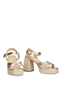 Zapatos de plataforma metálicos dorados con cuña de yute trenzado, que presentan correas de colores múltiples y hebilla en el tobillo. Superficie suave y suela texturizada.