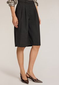 Tummanharmaat pleated culottes, jotka on valmistettu teksturoidusta kankaasta ja joissa on korkea vyötärö, viimeistelty valkoisella ompeluyksityiskohdalla. Yhdistetty kiiltäviin ruskeisiin korkokenkiin.