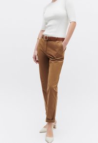 Pantaloni marrone su misura con risvolti, abbinati a una cintura beige. Indossati con una maglietta bianca a coste aderente e scarpe bianche con tacco a blocco.