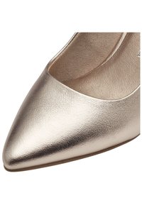 Μεταλλικό χρυσό γοβάκι με μυτερή μύτη, με εξωτερικό από λείο δέρμα και διακριτή υφή. Το εσωτερικό είνα ι επενδυμένο με μαλακό, ανοιχτόχρωμο υλικό.