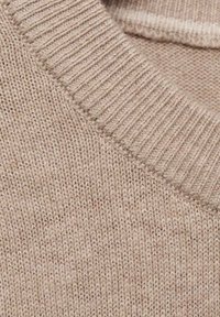 Lähikuva vaaleasta neulotusta kankaasta, jossa on ribbireuna ja yksityiskohtainen neulekuvio villapaidassa.