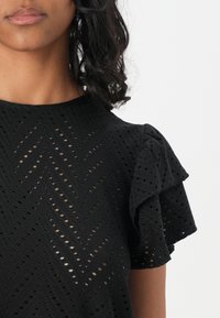 Blusa nera con un design texturizzato e motivi a intaglio, dotata di maniche corte a volant, realizzata in un tessuto leggero.