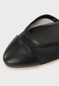 Chaussure plate noire avec un bout pointu, fabriquée en cuir lisse et en maille, dotée d'un intérieur rembourré et d'un design minimaliste.
