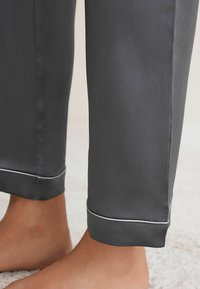 Grijze broek van gladde stof, met een opgerolde zoom met witte bies en een slim fit boven de enkel.