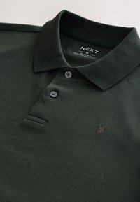 Ciemnozielona koszulka polo wykonana z teksturowanej tkaniny, z trzema guzikami, krótkimi rękawami i małym haftowanym logo jelenia na piersi.