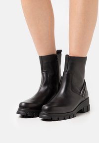 Stivali neri in pelle al polpaccio con punta tondeggiante, pannelli texture, chiusura con zip laterale e suola in gomma con battistrada spesso per la trazione.