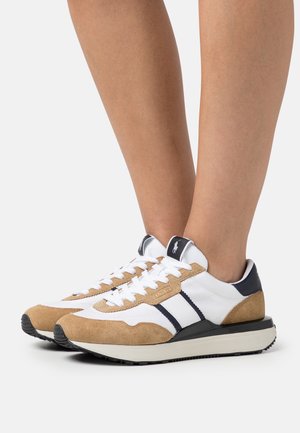 White and tan suede sneakers with black accents and laces worn on feet against a white background.