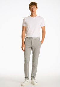 Heren lichtgrijze broeken van een gladde, gestructureerde stof, met een recht model, knoopsluiting en zijzakken, gecombineerd met een eenvoudige witte t-shirt.
