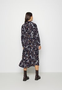 Vestido de manga longa em azul-marinho com um padrão floral em tons de azul, laranja e creme. Apresenta uma saia em camadas e é usado com botas de tornozelo escuras.