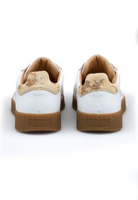 Weiße Ledersneaker mit einem Absatzdetail aus hellbraunem Wildleder und braunen Gummisohlen. Sie zeichnen sich durch ein schlichtes Design mit glatter Textur und dezenten Akzenten aus.