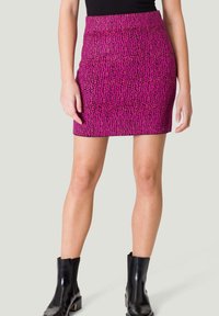 Mini-jupe rose à motif avec une surface texturée, une coupe ajustée et une taille haute. Assortie à des bottines noires pour le contraste.