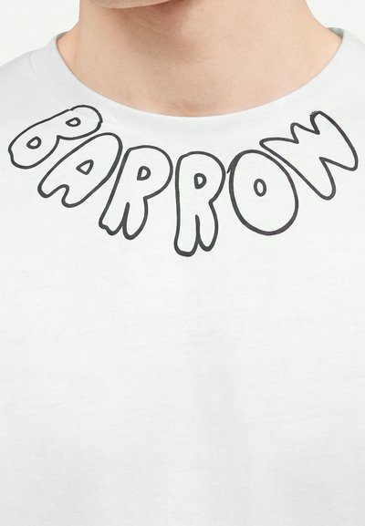 Gros plan sur un col de chemise blanche avec des lettres contour noir formant "BARROW" dans une police audacieuse et ludique.