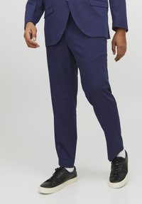 Marineblå skreddersydde bukser laget av glatt stoff, med slim fit og lommer, kombinert med svarte sneakers og hvite sokker.