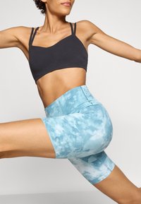 Black sports bra with thin straps paired with high-waisted blue tie-dye bicycle shorts, showcasing smooth texture and a fitted design.