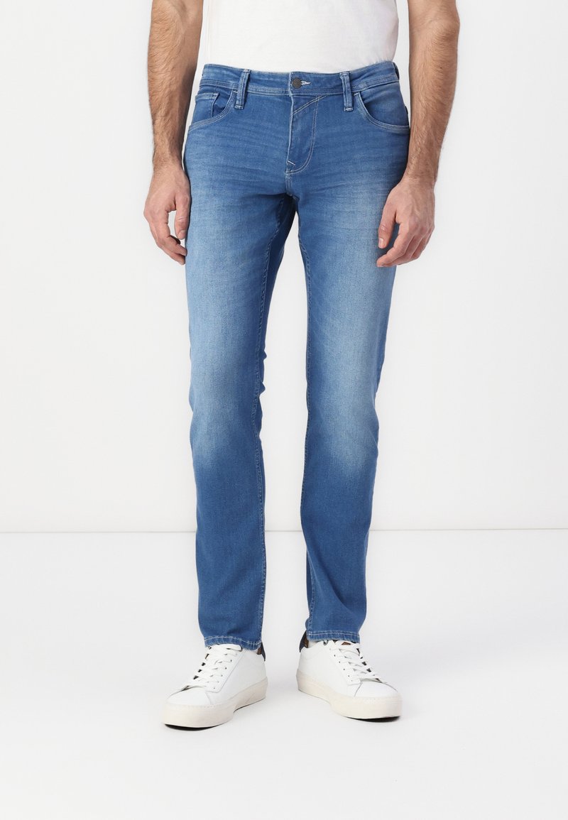 Vaqueros de denim azul con un corte ajustado, que presentan cinco bolsillos, un cierre de botón y cremallera, y ligeros desgastes en los muslos.