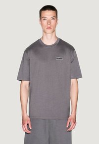 Camiseta gris de manga corta hecha de tela texturizada, con un discreto parche de logo en el pecho, con un corte relajado y cuello redondo.