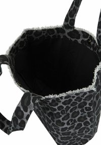 Sac fourre-tout avec un imprime léopard noir et gris foncé, bords effilochés, deux poignées et un intérieur en tissu noir ouvert avec fermeture à bouton-pression.