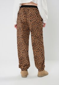 Hlače s leopard uzorkom u nijansama smeđe i crne, s elastičnom pasicom i manžetama, izrađene od mekanog materijala.