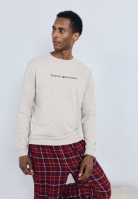 Sudor verde deschis cu guler rotund și mâneci lungi, având logo-ul "TOMMY HILFIGER" în albastru închis și roșu. Asortat cu pantaloni de pijama roșii cu carouri.