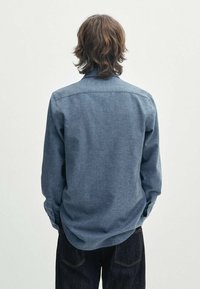 Denimhemd in Mittelblau mit langen Ärmeln, Button-Down-Kragen und geradem Rückenpasse. Verfügt über einen strukturierten Stoff und eine lässige Passform.