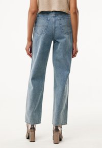 Jeans de tiro alto en azul claro con un diseño de pierna recta, cuatro bolsillos y una textura descolorida, combinados con zapatos de tacón metálicos.