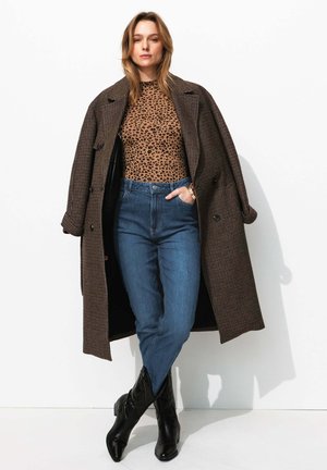 Manteau marron en pied-de-poule sur un top beige à imprimé léopard, associé à un jeans bleu taille haute et des bottines noires, avec une texture lisse.