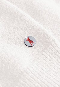 Circulaire zilveren badge met een rode silhouet van een hond op een gestructureerde witte stoffen achtergrond.