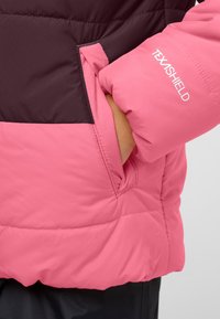 Vadderad jacka med en färgblockdesign i rosa och mörklila. Har en fleece-fodrad ficka och "TEXASHIELD"-logotyp på ärmen.