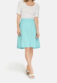 Una falda de color turquesa claro con un diseño acampanado, hecha de algodón, que presenta una cintura elástica. Combinada con una blusa blanca ajustada de manga corta.