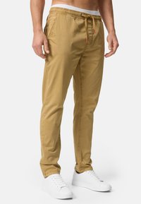Chinos de algodón beige con cintura elástica, acento de cordón, bolsillos laterales, piernas ajustadas y detalles cosidos. Combinados con zapatillas blancas.