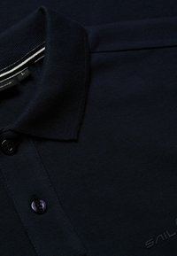 Marinblå polo skjorta i strukturerad tyg, med en treknappslukning, klassisk krage och subtila vita randade detaljer på kragen.