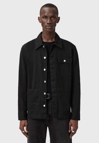 Czarna kurtka z tkaniny z kołnierzykiem, z przodu zapinana na guziki, z dwiema przednimi kieszeniami i kieszenią na piersi. Dopasowany krój z lekko teksturowanym wykończeniem.