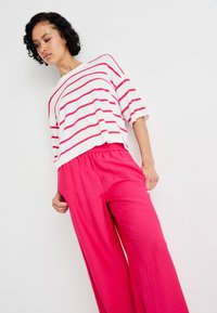 White sweater with horizontal pink stripes, paired with loose-fitting pink trousers. Casual design and soft texture, featuring wide legs.
