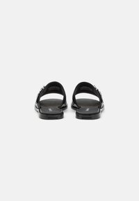 Svarta platta sandaler med en stilren design, öppen bak och en slät yta. Inkluderar en silverfärgad spänneaccent på sidan.