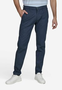 Pantalon bleu marine en tissu texturé, avec une coupe standard, des poches latérales et une fermeture à bouton, associé à des baskets blanches.