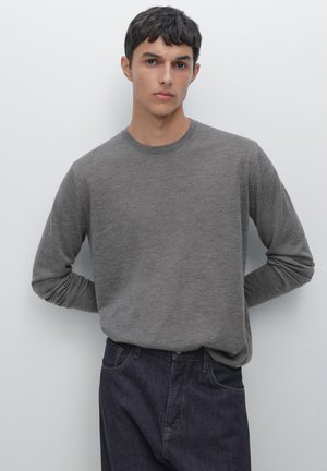 Grey long-sleeve crewneck sweater made of soft knit fabric, worn with dark denim jeans. The texture is smooth with a casual design.
