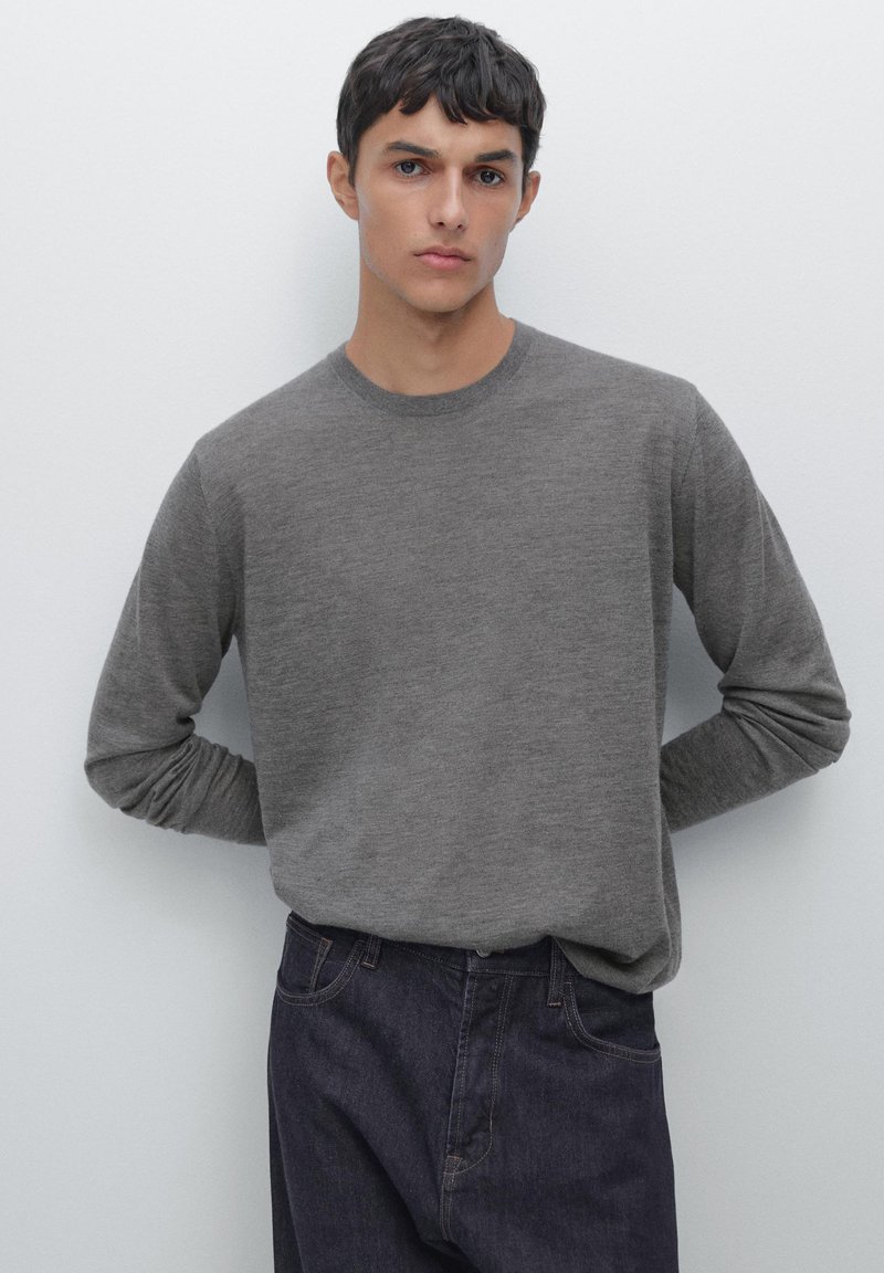 Maglione grigio a maniche lunghe con collo rotondo, realizzato in morbido tessuto knit, indossato con jeans di denim scuro. La texture è liscia e dal design casual.