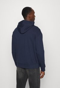 Navy blue hoodie made of cotton blend, featuring a kangaroo pocket, ribbed cuffs, and a slightly cropped design. Textured, soft fabric.