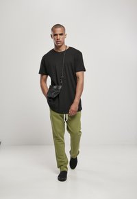 Zwarte kortemouwt-shirt gecombineerd met groene joggingbroek, met een elastische tailleband. Zwarte schoudertas, gedragen aan de linkerkant, voegt detail toe.